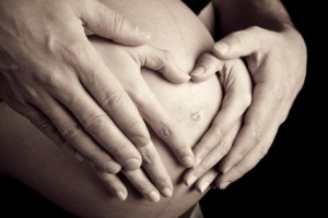 hands of pregnant woman and her husband in heart shape on her be
